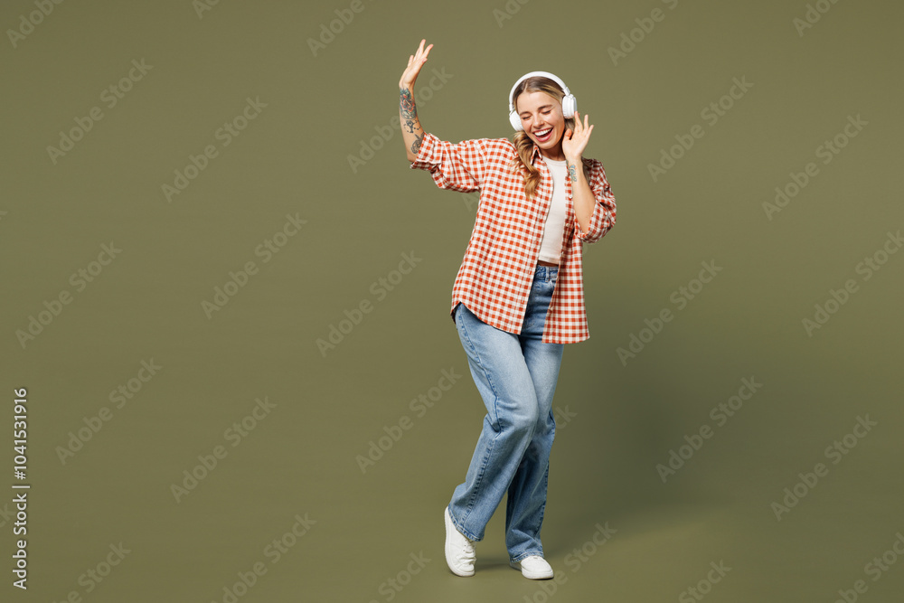 Full body young smiling happy woman wear red shirt white t-shirt casual clothes listen to music in headphones raise up hands dance isolated on plain pastel green background studio. Lifestyle concept. Full body young smiling happy woman wear red shirt white t-shirt casual clothes listen to music in headphones raise up hands dance isolated on plain pastel green background studio. Lifestyle concept.