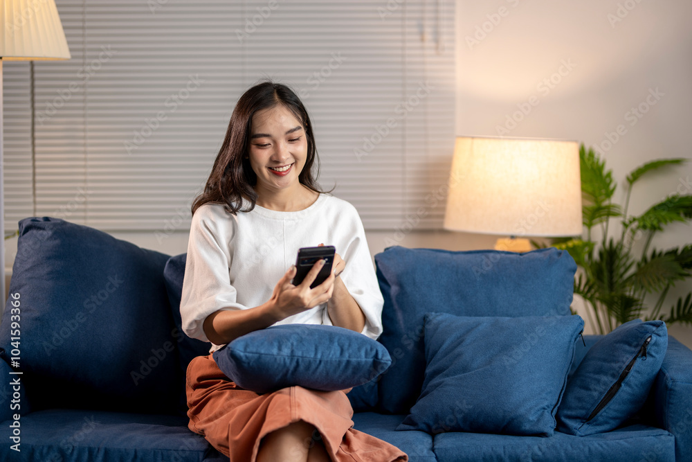 Fototapeta premium Young woman relaxing on sofa at home using smartphone browsing internet