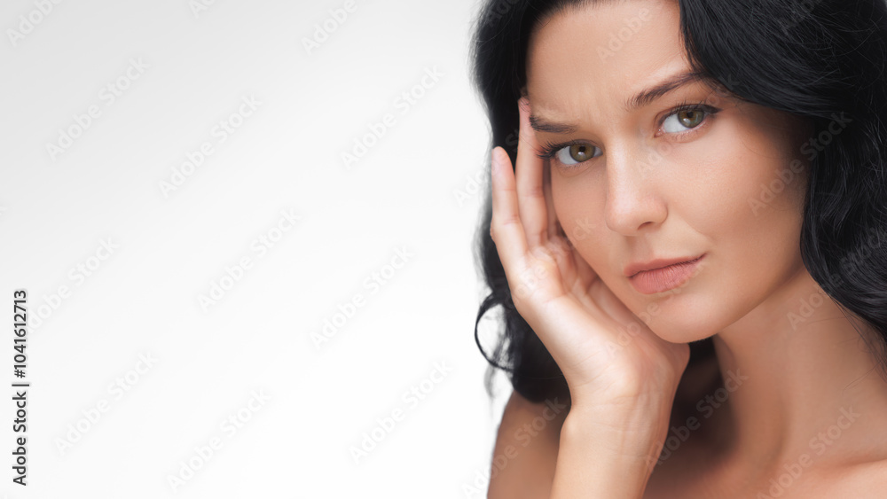 A thoughtful Asian woman with long black hair and flawless skin touches her face with a concerned expression against a neutral background. Perfect for beauty, skincare, and health-related promotions A thoughtful Asian woman with long black hair and flawless skin touches her face with a concerned expression against a neutral background. Perfect for beauty, skincare, and health-related promotions