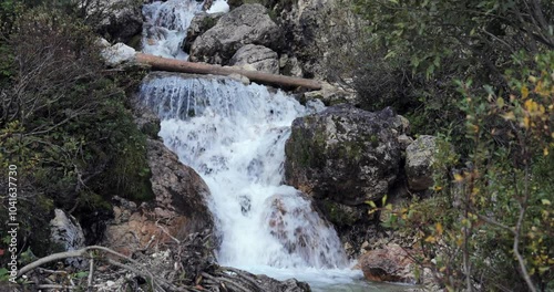 A fast stream of water from Cascate del Pisciadu descends over a rocky bed. The waterfall is set amidst alpine vegetation in the Dolomites, Italy photo