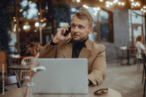 young beard man working on a laptop sitting at cafe write messages to drinking coffee smiling typing on a keyboard computer surfing smart phone, business suit, autumn moods, using smartphone in hand