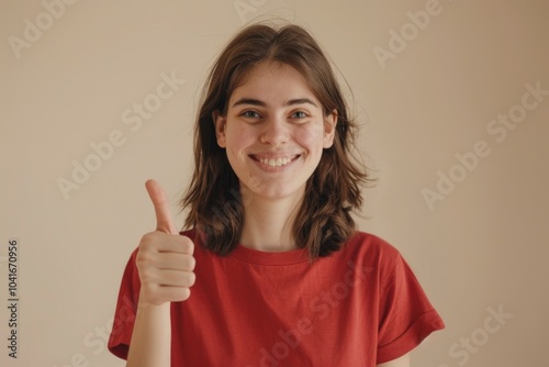 A young woman wearing a bright red shirt gives a thumbs up, conveying positivity and confidence