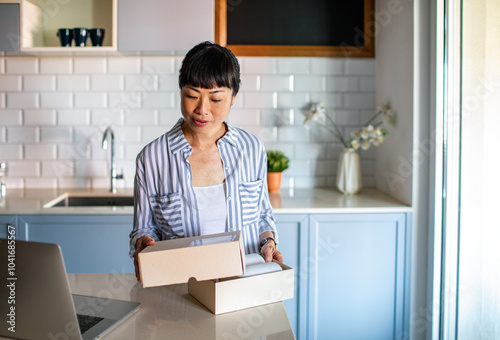 Smiling Asian woman opening package at home with laptop