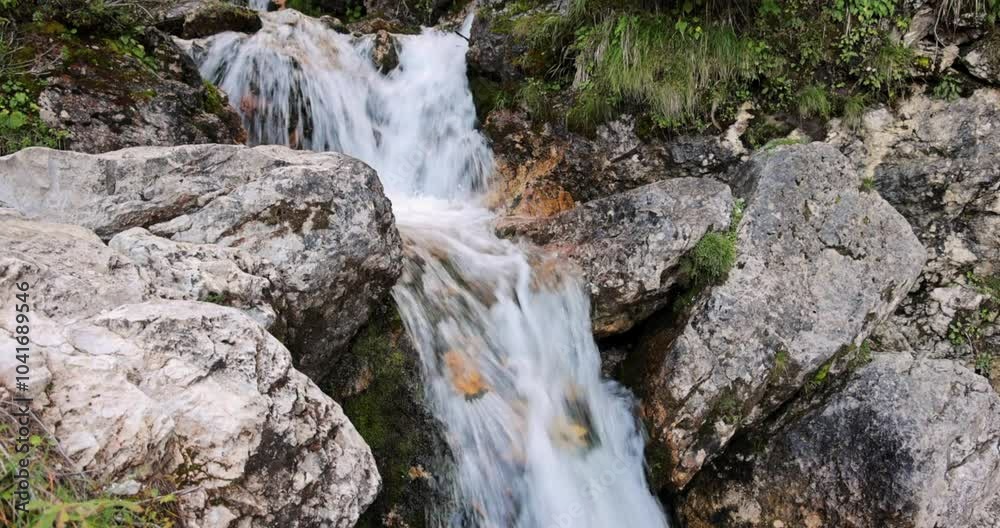 Stream of water rushes over rocks in the Pisciadu waterfalls, located in the Dolomite Alps of Italy. The shot highlights the dynamic motion of water amid rugged stone formations