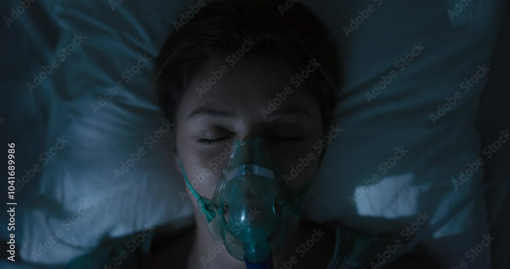 Female patient in oxygen mask in hospital bed recovers.