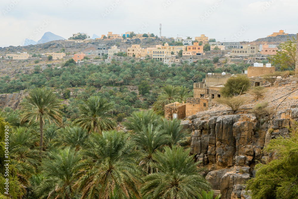 Traditional village nestled among palm trees in the mountainous landscape of Oman during daylight Traditional village nestled among palm trees in the mountainous landscape of Oman during daylight