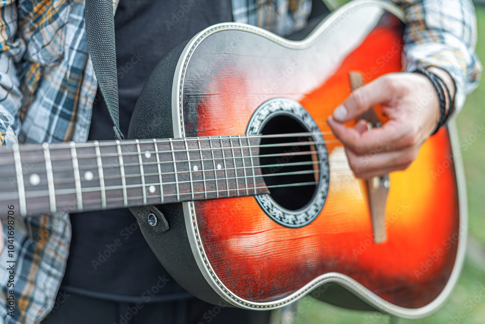 Male hands with an acoustic guitar against a background of a country landscape.
