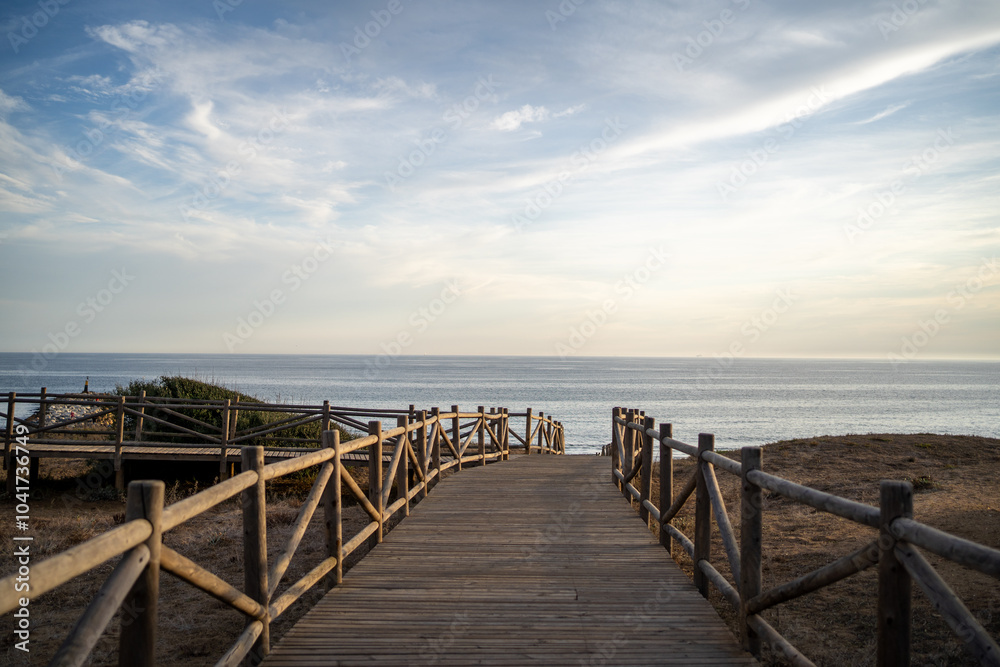 A wide-angle view of a peaceful beach and ocean as the sun sets behind distant hills, casting a warm glow over the coastline and sea A wide-angle view of a peaceful beach and ocean as the sun sets behind distant hills, casting a warm glow over the coastline and sea