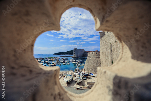 A glimpse of the vibrant harbor of Dubrovnik Croatia framed by an ancient stone window on a sunny day