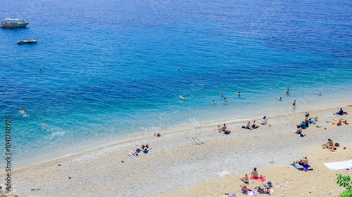 Fototapeta Naklejka Na Ścianę i Meble -  Relaxing beach day in the crystal clear waters of Dubrovnik Croatia with sunbathers enjoying the warm summer sun by the shore