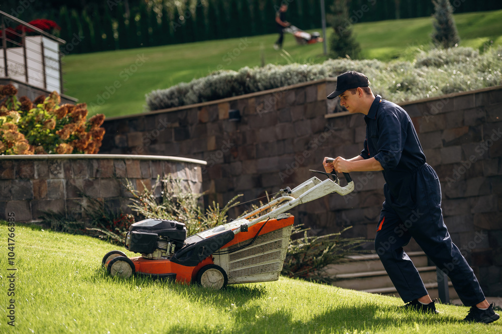 View from the side, cutting grass by lawn mover. Professional gardener is on the lawn View from the side, cutting grass by lawn mover. Professional gardener is on the lawn