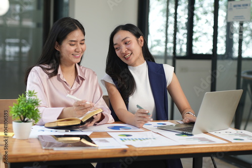 Happy Asian business people working together using laptop and tablet in office.