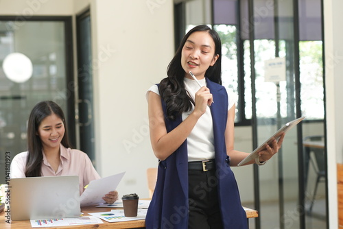 Happy Asian business people working together using laptop and tablet in office.