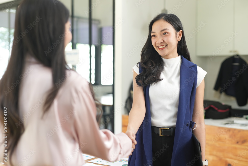Obraz premium Two female managers happily shake hands in an office meeting.