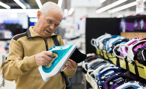 Elderly man choosing iron in showroom of electrical appliance store