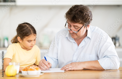 Father helping little daughter do school homework in kitchen