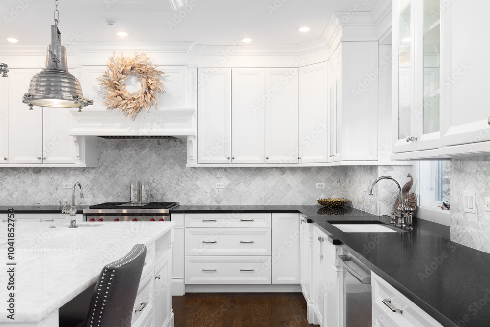 A white kitchen with white and black marble countertops, pendant light ...