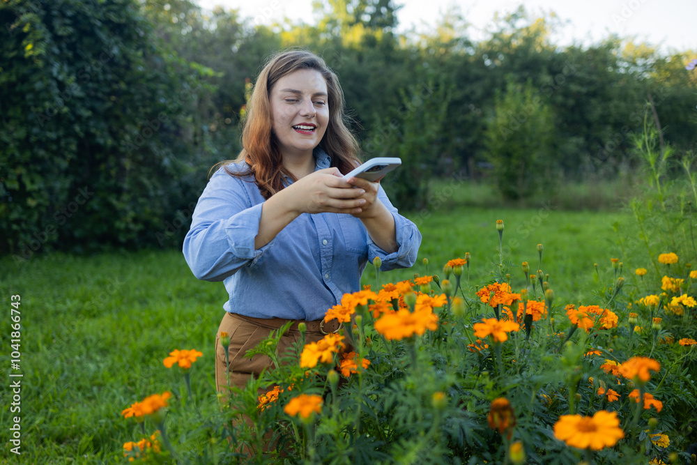 Shot of an happy female Caucasian farmer working in her yard using a phone and taking a photo. Gardener using mobile phone. The concept of gardening, growing and caring for flowers and plants.