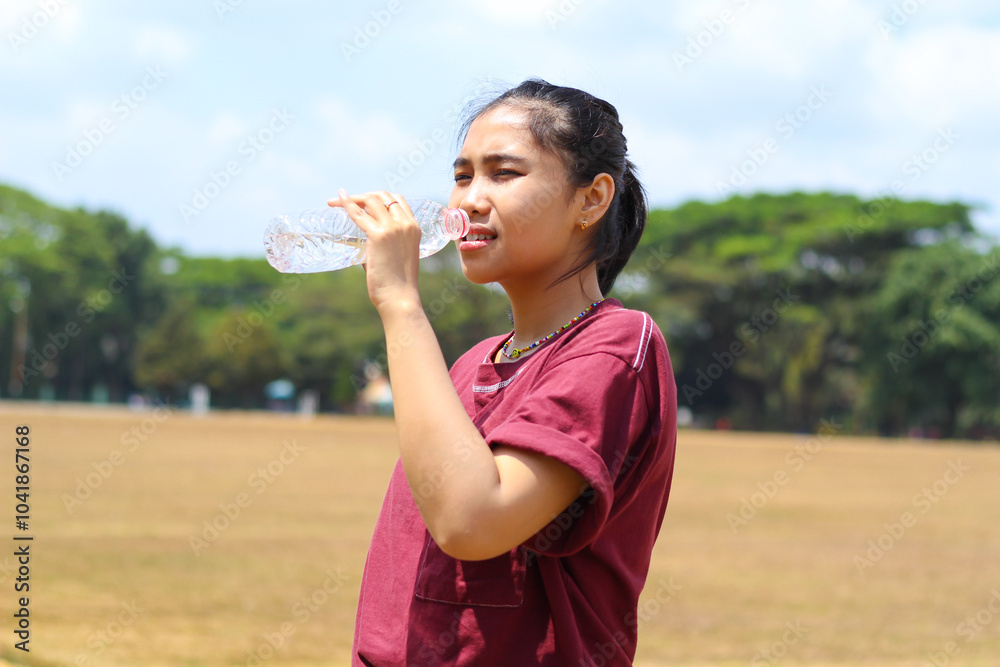 asian woman drink a bottle of water after running in outdoors in midday wearing casual t shirt asian woman drink a bottle of water after running in outdoors in midday wearing casual t shirt