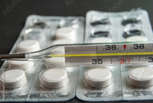 A close-up shot of a thermometer and paracetamol pills isolated on a black background, ideal for illustrating health, medicine, and seasonal flu concepts. photo