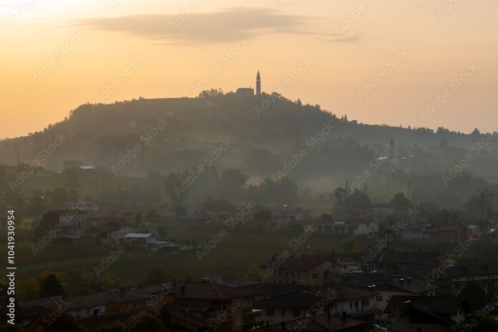 La silhouette del borgo di Formeniga, in provincia di Treviso, Veneto, Italia, contro il cielo arancione all'alba di un giorno d'autunno, lungo il cammino delle colline del Prosecco La silhouette del borgo di Formeniga, in provincia di Treviso, Veneto, Italia, contro il cielo arancione all'alba di un giorno d'autunno, lungo il cammino delle colline del Prosecco