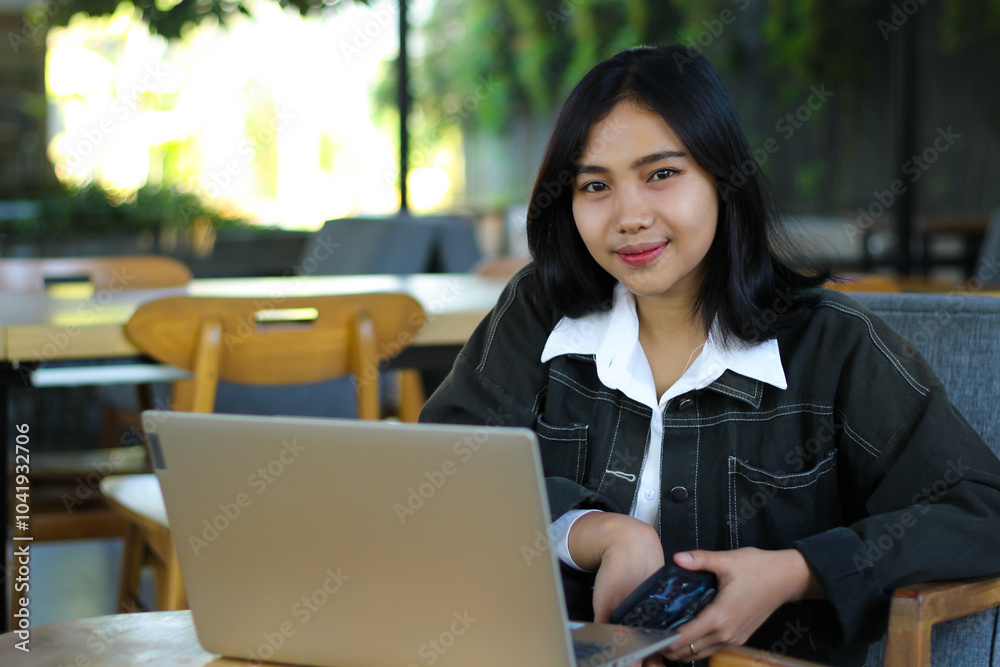 pretty asian woman using laptop in cafe and holding smartphone looking at camera with confidence and elegant smile pretty asian woman using laptop in cafe and holding smartphone looking at camera with confidence and elegant smile