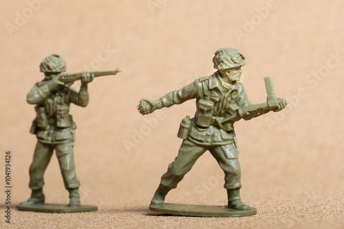 Toy soldier figures (ww2 era uniforms), green plastic, one providing covering fire, the other advancing with grenade, isolated against a sandy colour background.