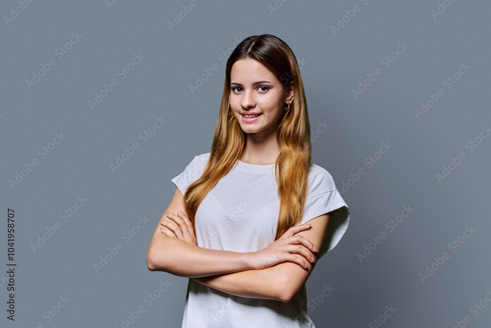Fototapeta premium Beautiful young girl with crossed arms looking at camera on gray background