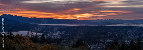 Panoramic view of sunrise over Fraser Valley at Port Moody, BC, with low-lying cloud inversions on valley floor and mountains in silhouette on horizon. photo