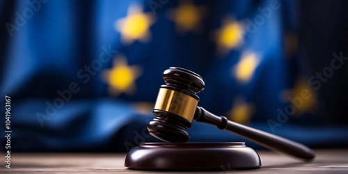 The European Union flag waving in the background, with a close-up of a wooden gavel, evoking the themes of legal authority, justice, and the power of law within the EU. photo