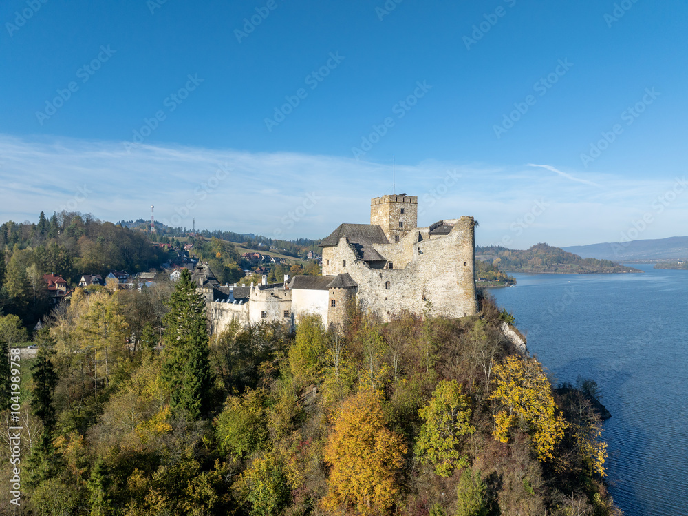 Poland. Medieval castle in Niedzica, dating to 14th century (upper castle) in autumn in October. Trees in beautiful fall colors. Sunset light. Artificial Czorsztyn lake on Dunajec river. Aerial view