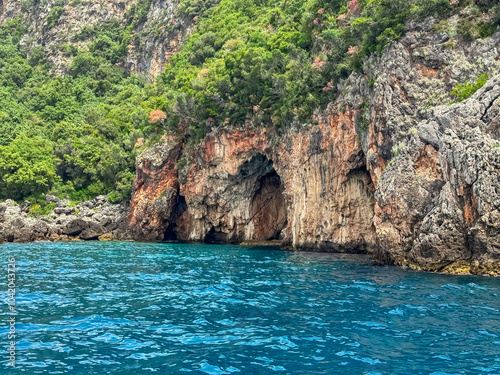 Boat trip with scenic view of large sea cave called Monastery caves near Himare, Vlore, Albania. Dramatic coastal landscape of Albanian Riviera with natural archway. Sightseeing on Mediterranean sea photo