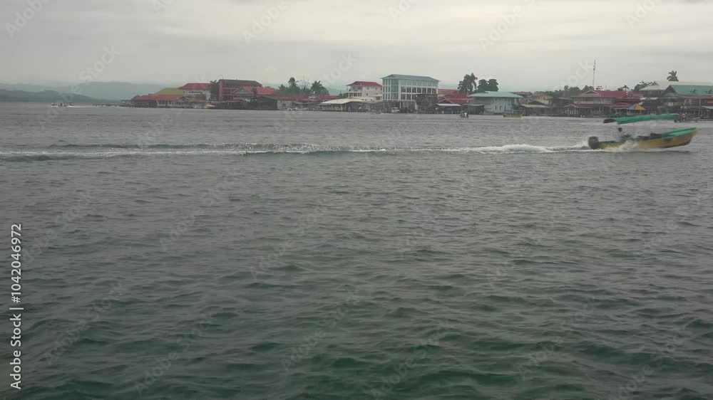 Boats pass a tropical island with buildings on the shoreline during a cloudy day Boats pass a tropical island with buildings on the shoreline during a cloudy day