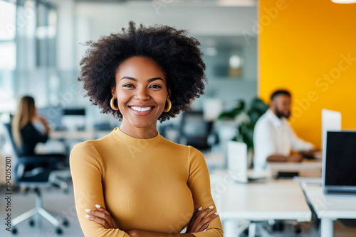 A woman with curly hair is smiling and posing for a picture in a cubicle