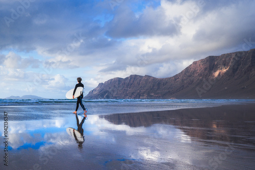 An athletic surfer walks the beach with a surfboard during sunset, famara beach, Lanzarote, Canary Islands, Spain photo