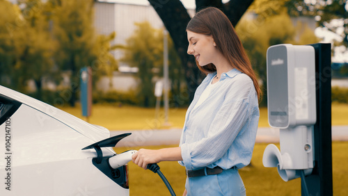 Woman recharging battery for electric car during road trip travel EV car in autumanl season natural forest or national park. Eco friendly travel during vacation and holiday. Exalt photo