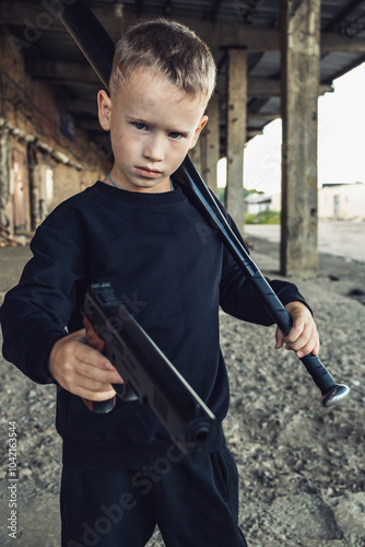 A boy in black clothes with a baseball bat and a gun in his hands.