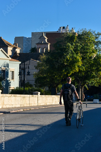 Wallpaper Mural A bald, casually dressed man, with his back turned, pushing a bicycle down a street in a European city Torontodigital.ca
