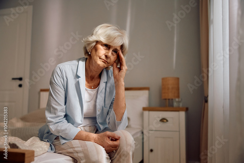 Sad senior woman sitting alone on bed.