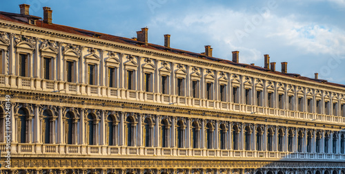 The New Procuracie showcases stunning Venetian architecture, featuring intricate columns and detailed facades under a bright sky, reflecting the historical beauty of Venice at sunset. #1042248149