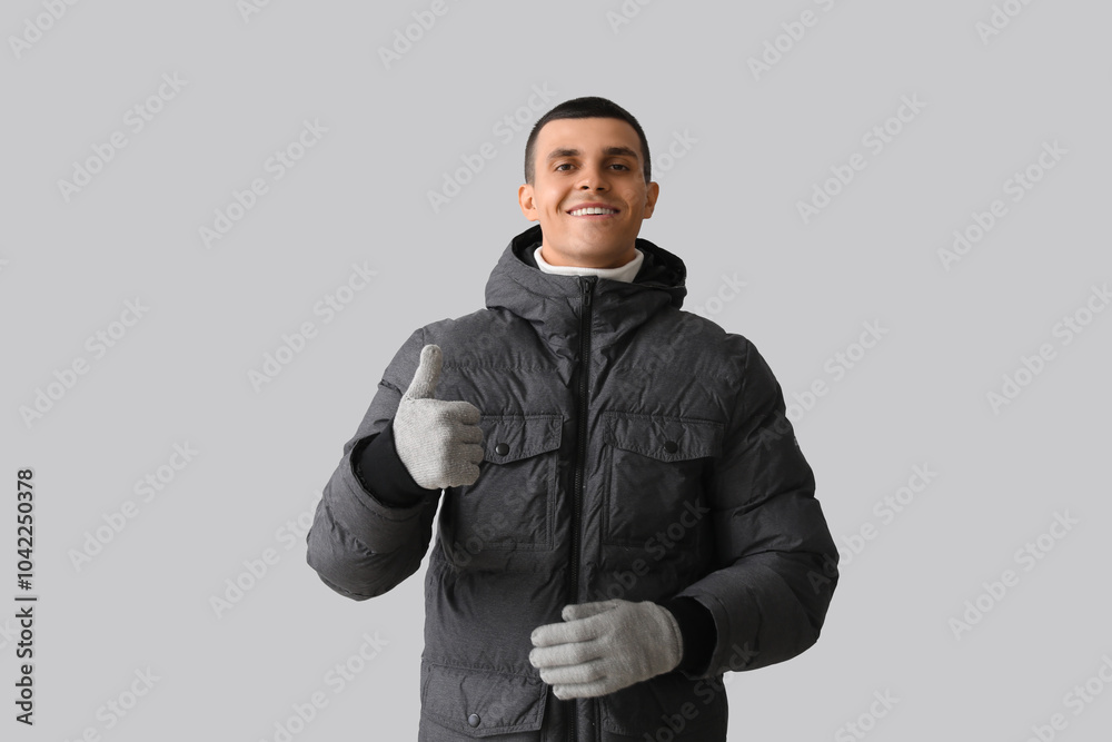 Young man in puffer jacket showing thumb-up on light background Young man in puffer jacket showing thumb-up on light background