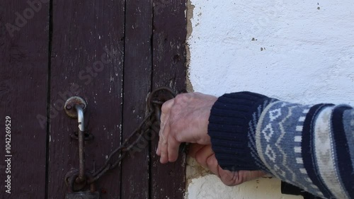 A man opens a padlock on a wooden door with a key.