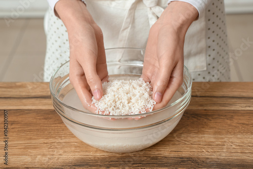 Foto Woman rinsing rice in glass bowl near wooden table, closeup