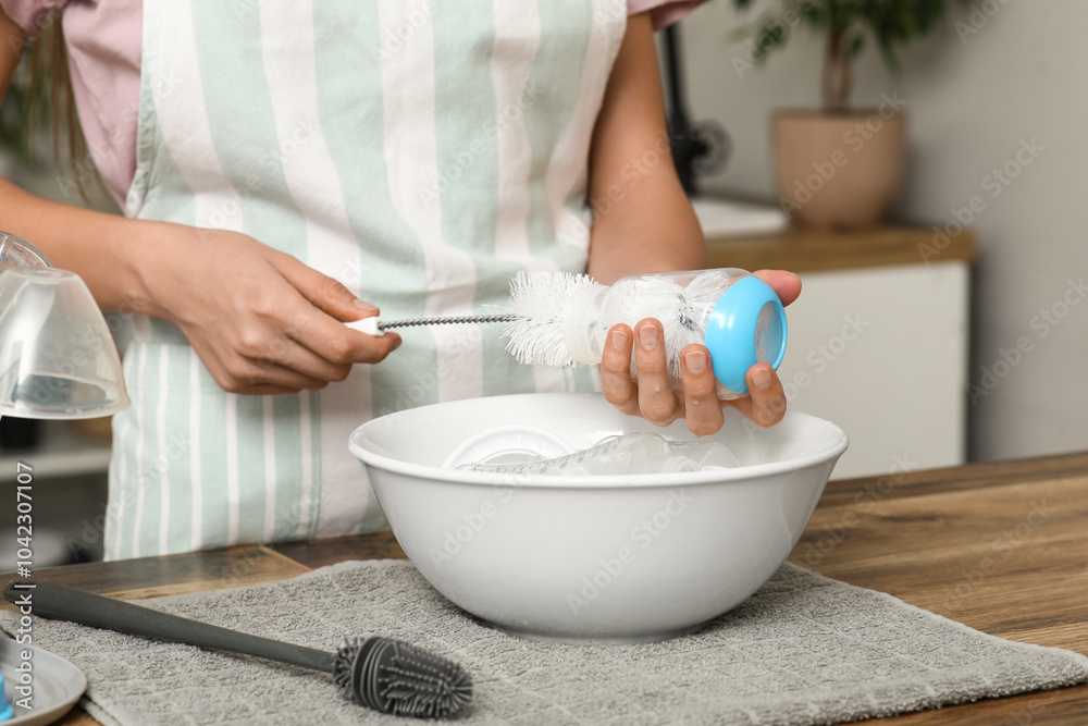 Woman with brush cleaning baby bottle at counter in kitchen, closeup Woman with brush cleaning baby bottle at counter in kitchen, closeup