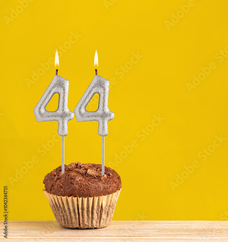 Number 44 birthday candle - Chocolate cupcake on a yellow background.