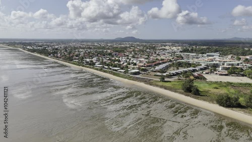Drone flies over beach on Atlantic Ocean at low tide toward city center in Kourou, French Guiana, France