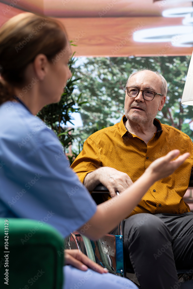 Nurse explaining disease diagnosis to elderly man in wheelchair, providing support and medical treatment during home visit. Caretaker consulting senior patient with disability. Nurse explaining disease diagnosis to elderly man in wheelchair, providing support and medical treatment during home visit. Caretaker consulting senior patient with disability.