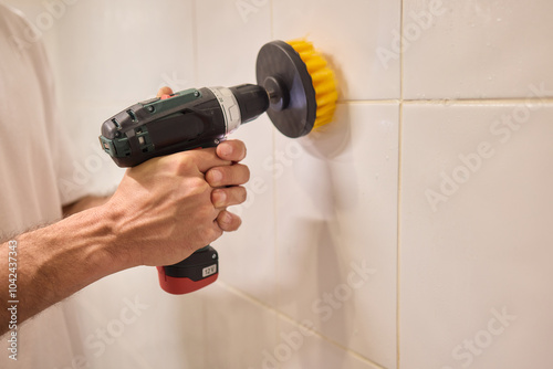 A man is using an electric drill that has a brush attachment to thoroughly clean tiles