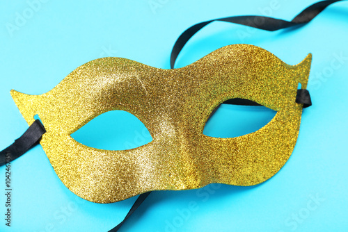 One golden carnival mask on light blue background, closeup