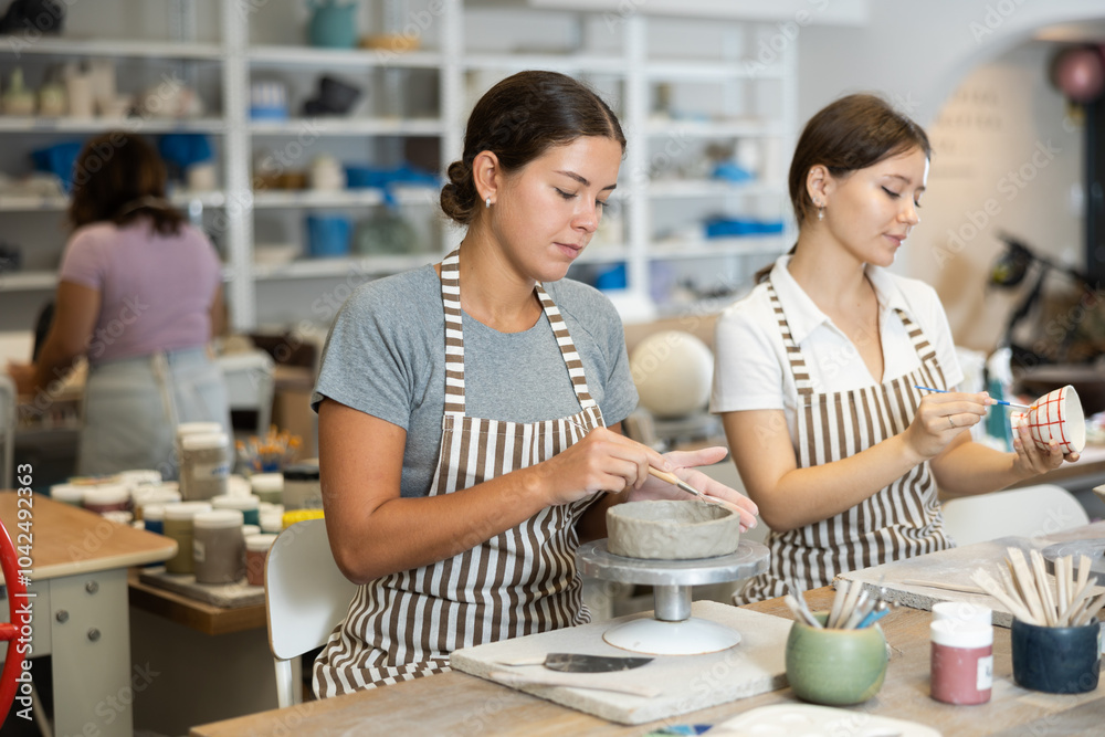 Fototapeta premium Young woman teacher and young girl student sculpt and paint ceramics in workshop